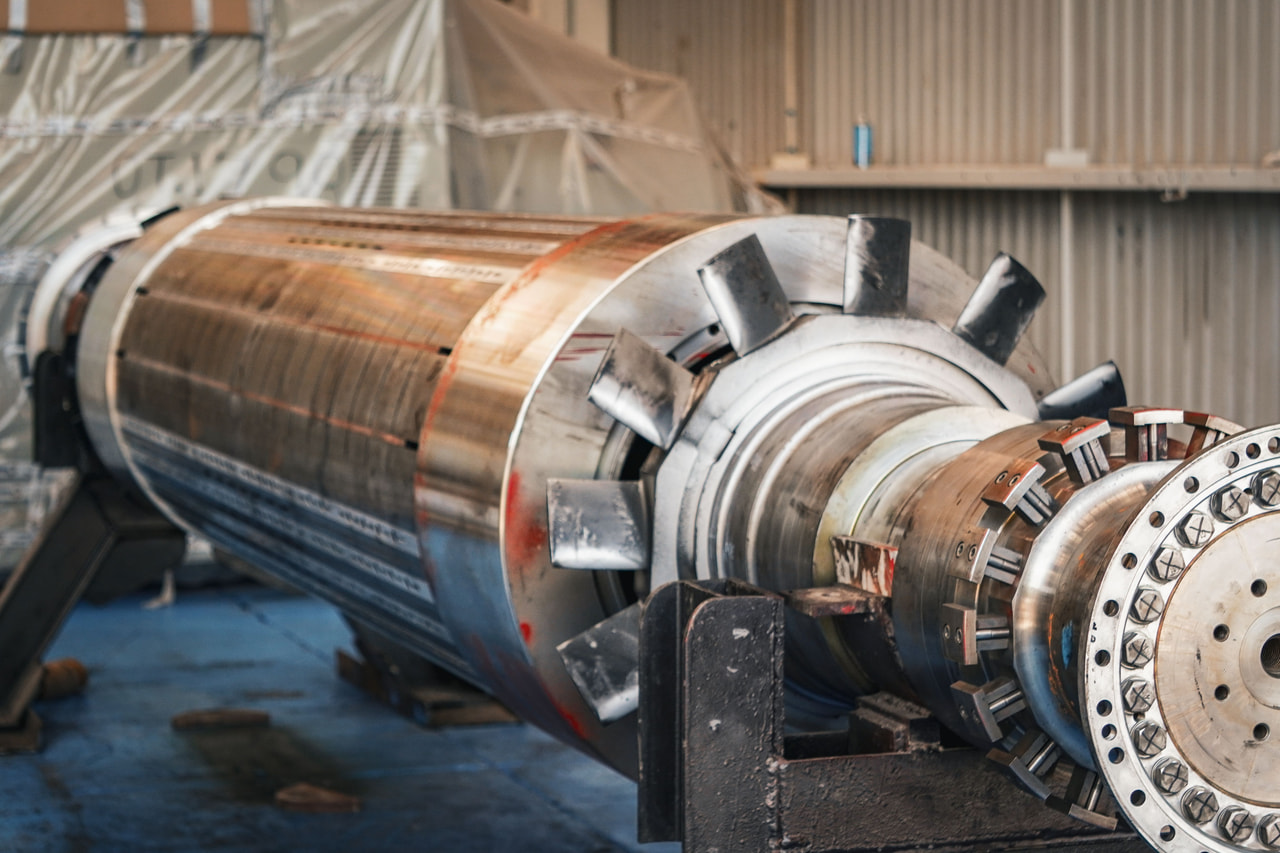Large generator rotor shaft with fan blades resting on workshop stands